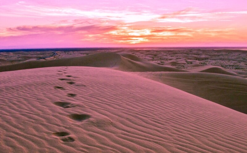 Footprints in sand against a pink sunset