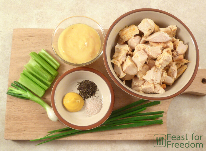 Ingredients needed to make chicken salad on a cutting board - chicken, celery, green onions, mayonnaise, mustard, salt and pepper