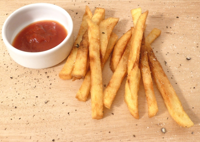 Homemade French Fries on a wooden board next to a small dish of ketchup