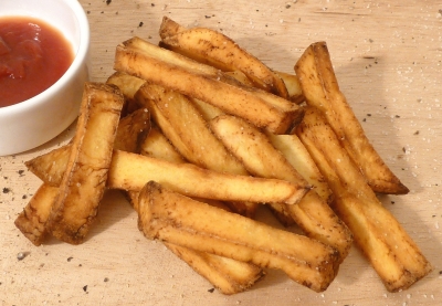 French fries on a board, sprinkled with seasoning, next to a bowl of ketchup