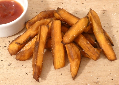 Sweet potato fries on a board, sprinkled with seasoning, next to a bowl of ketchup