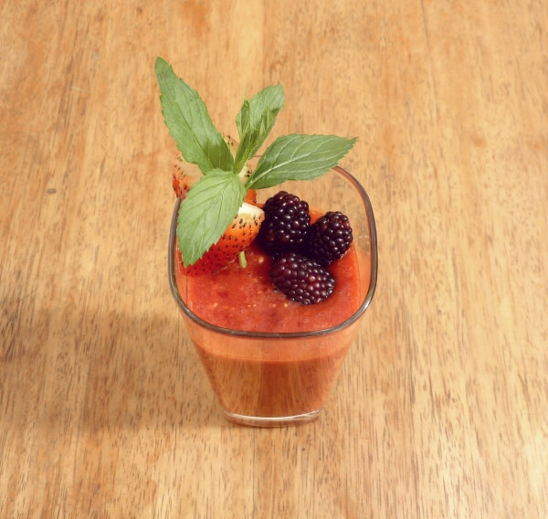 Strawberry, blackberry and peach fruit smoothie in a tall glass with a fresh strawberry and blackberry garnish