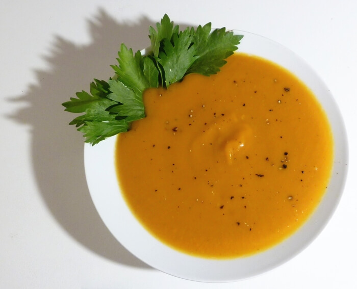 Ginger squash soup in a bowl with a sprig of parsley and fresh ground pepper.