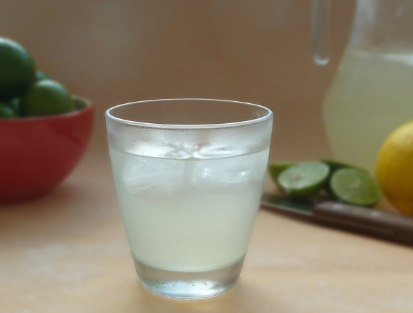Lemonade in a glass next to lemons and limes