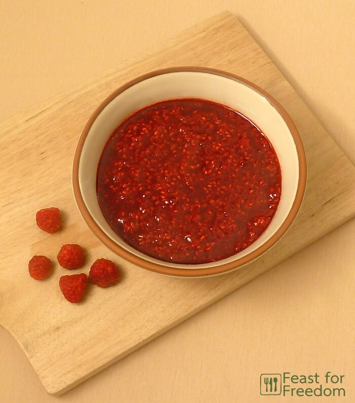 Raspberry sauce in a bowl with some fresh raspberries next to it