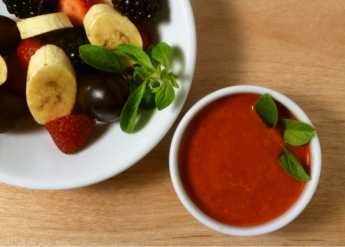 Raspberry dressing in a little dish next to a fruit salad