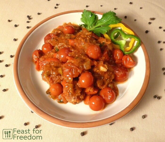Meatballs with cherry tomato sauce on a plate garnished with sweet peppers and celery leaves